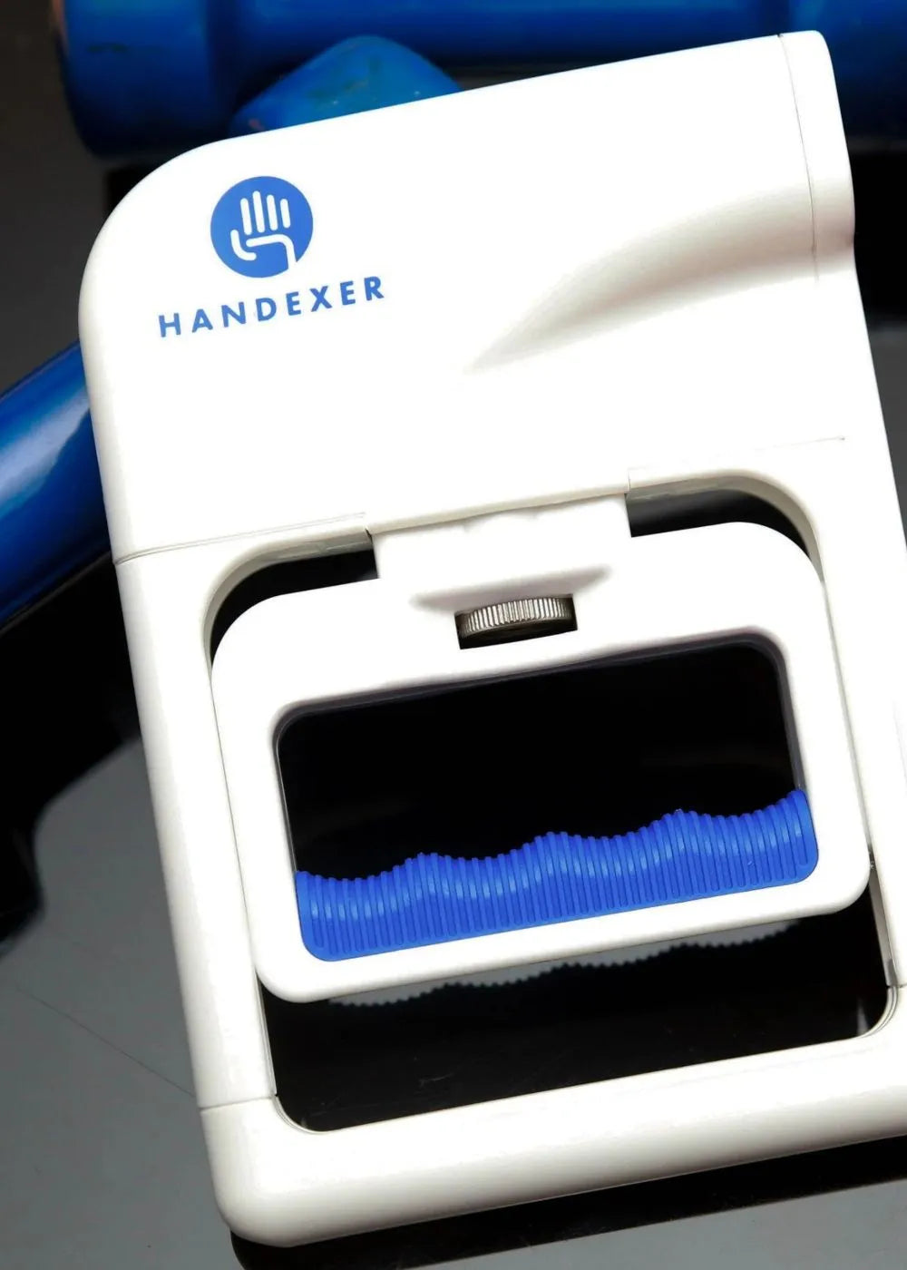 A close - up of the Handexer grip strength hand dynamometer. The device is white with a blue Handexer logo on the top. It features a blue grip area and a silver adjustment knob, designed as a tool to measure grip strength.