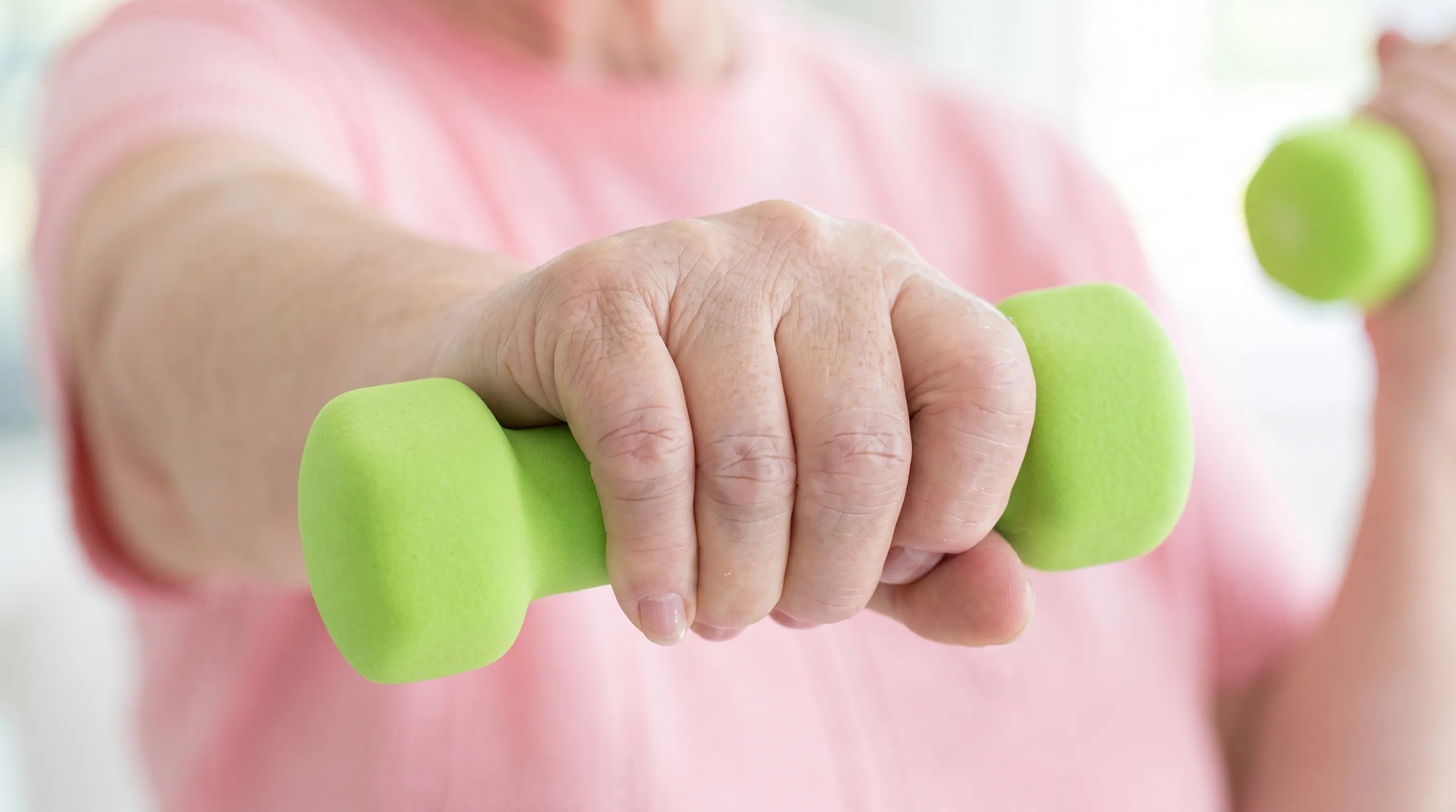 Handexer senior hand strength training, close‑up of elderly hands gripping light dumbbells for hand and forearm rehabilitation workout at home.