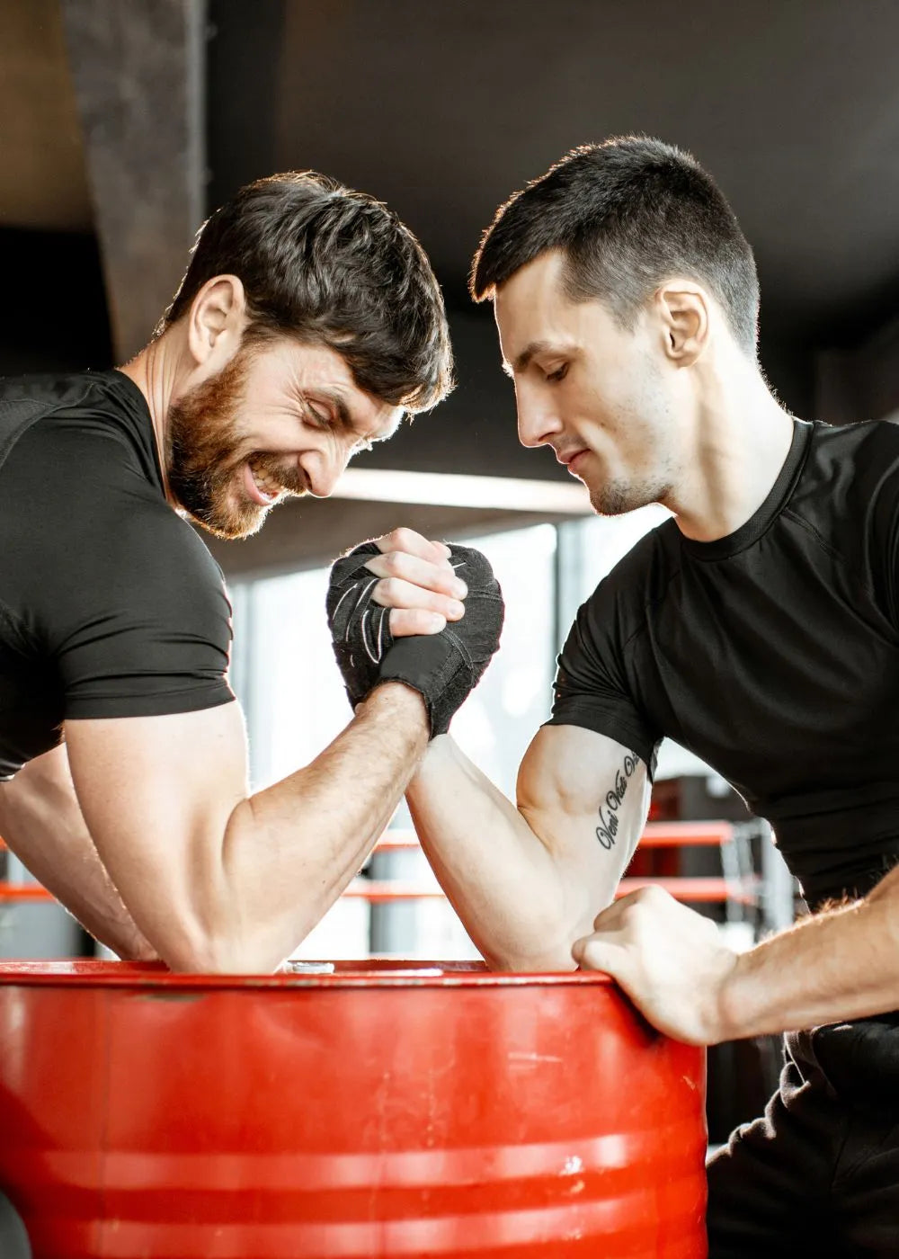Two individuals engaged in an arm - wrestling match, showcasing hand grip strength. This image is relevant for grip strength measurement tools like the Grip Strength Hand Dynamometer. The setting appears to be a gym - like environment, emphasizing isometric handgrip exercises.