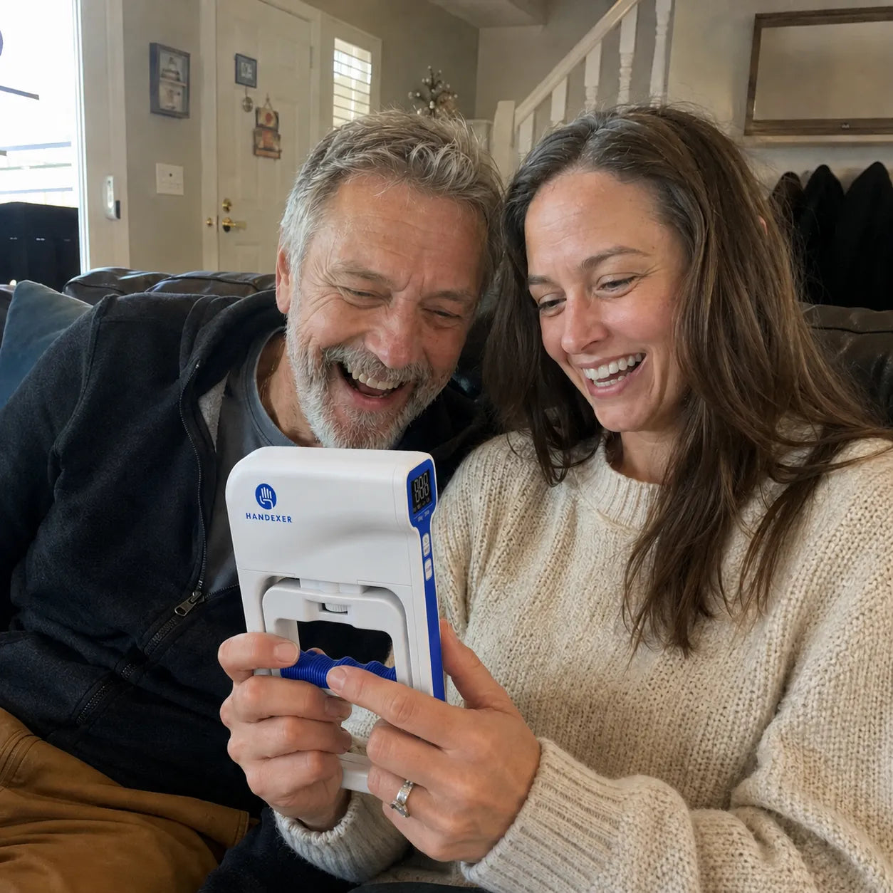 Smiling couple using a Handexer digital hand dynamometer together on a sofa in a casual home setting